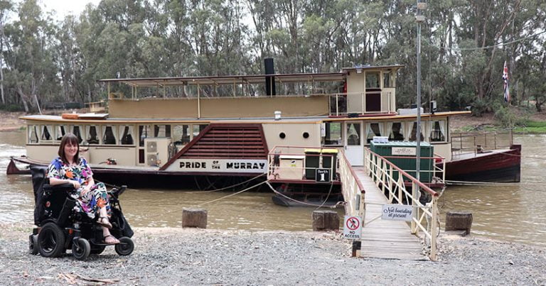 A young woman in a wheelchair in front of a paddle steamer