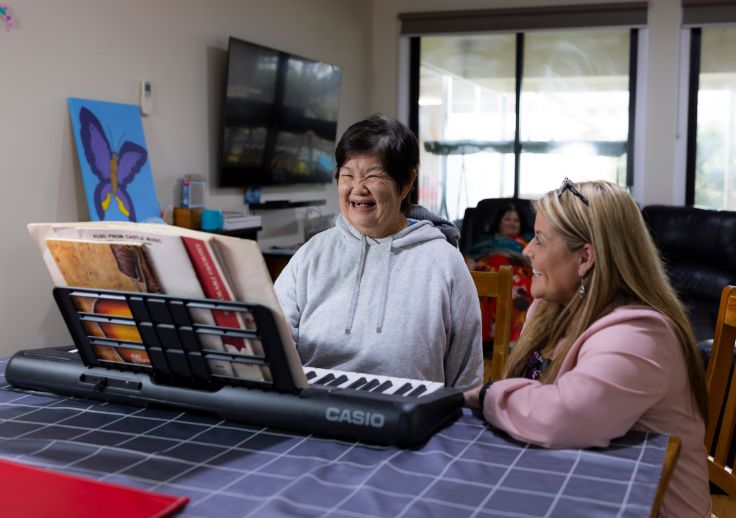 A ndis participant using the keyboard with their Aruma support worker by their side.